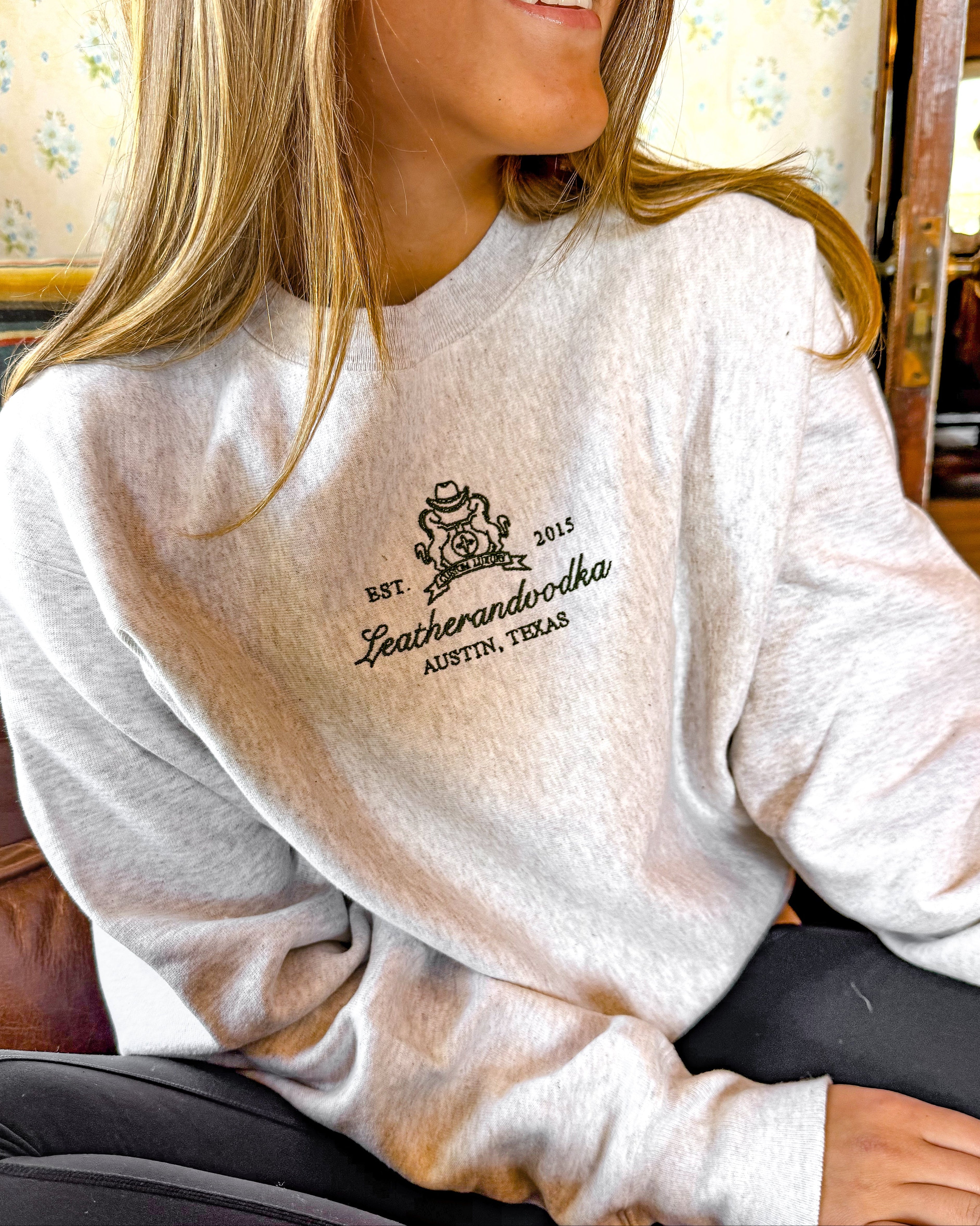 Person wearing a white sweatshirt with a logo and text, sitting indoors.