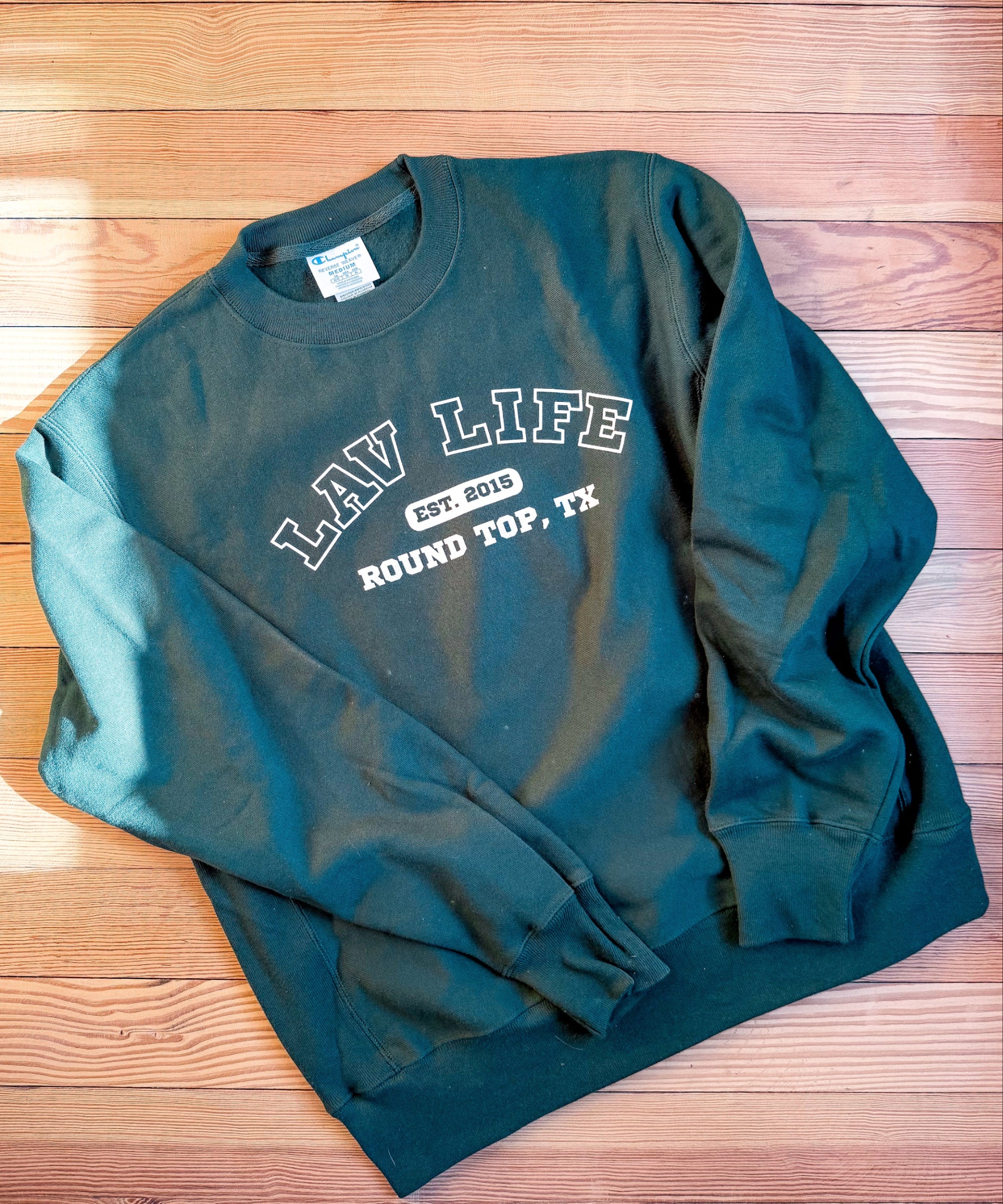 Green sweatshirt with LAV Life, Round Top, Texas text on a wooden surface