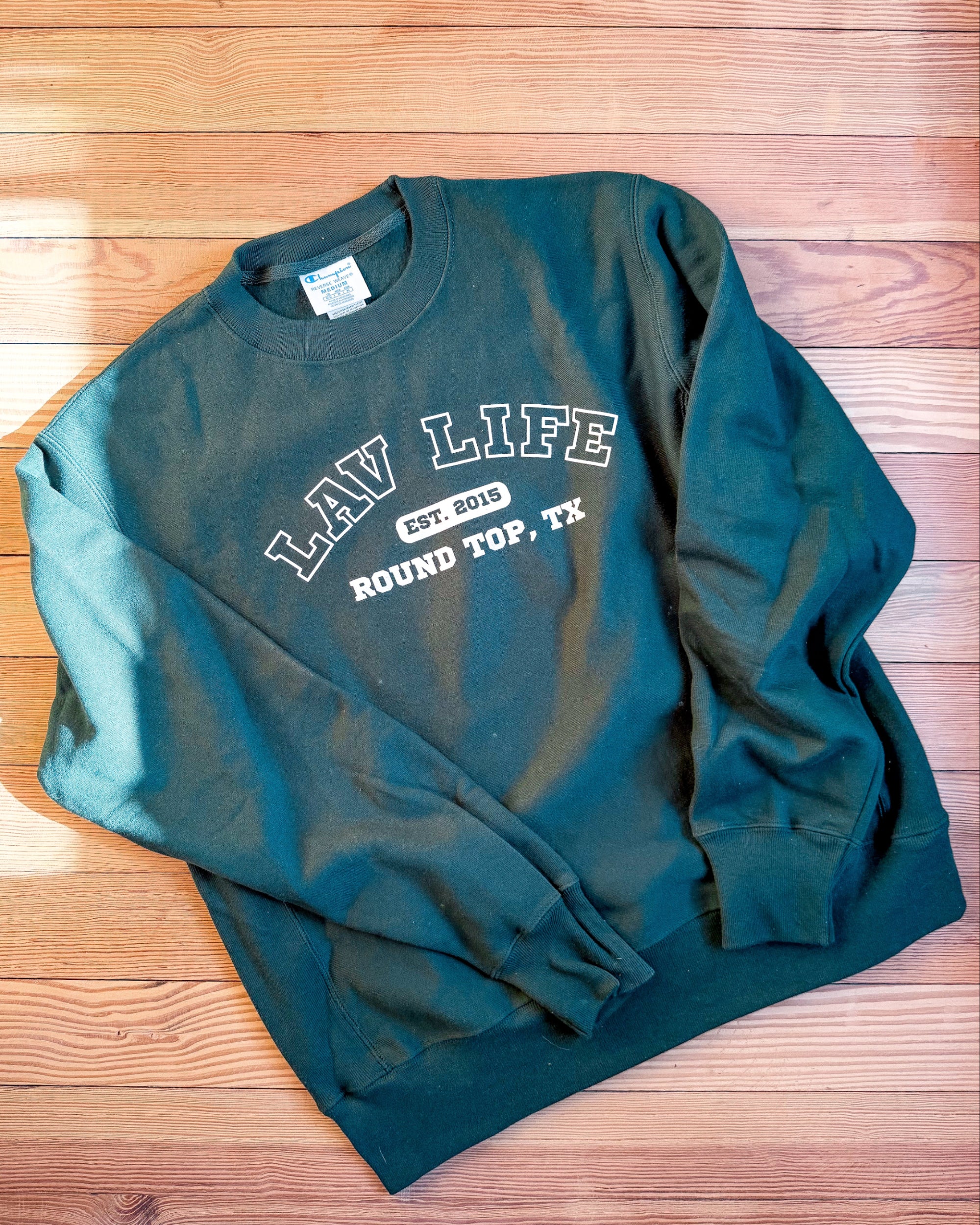 Green sweatshirt with LAV Life, Round Top, Texas text on a wooden surface