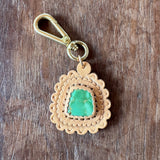 Gold keychain with a green gemstone on a wooden surface