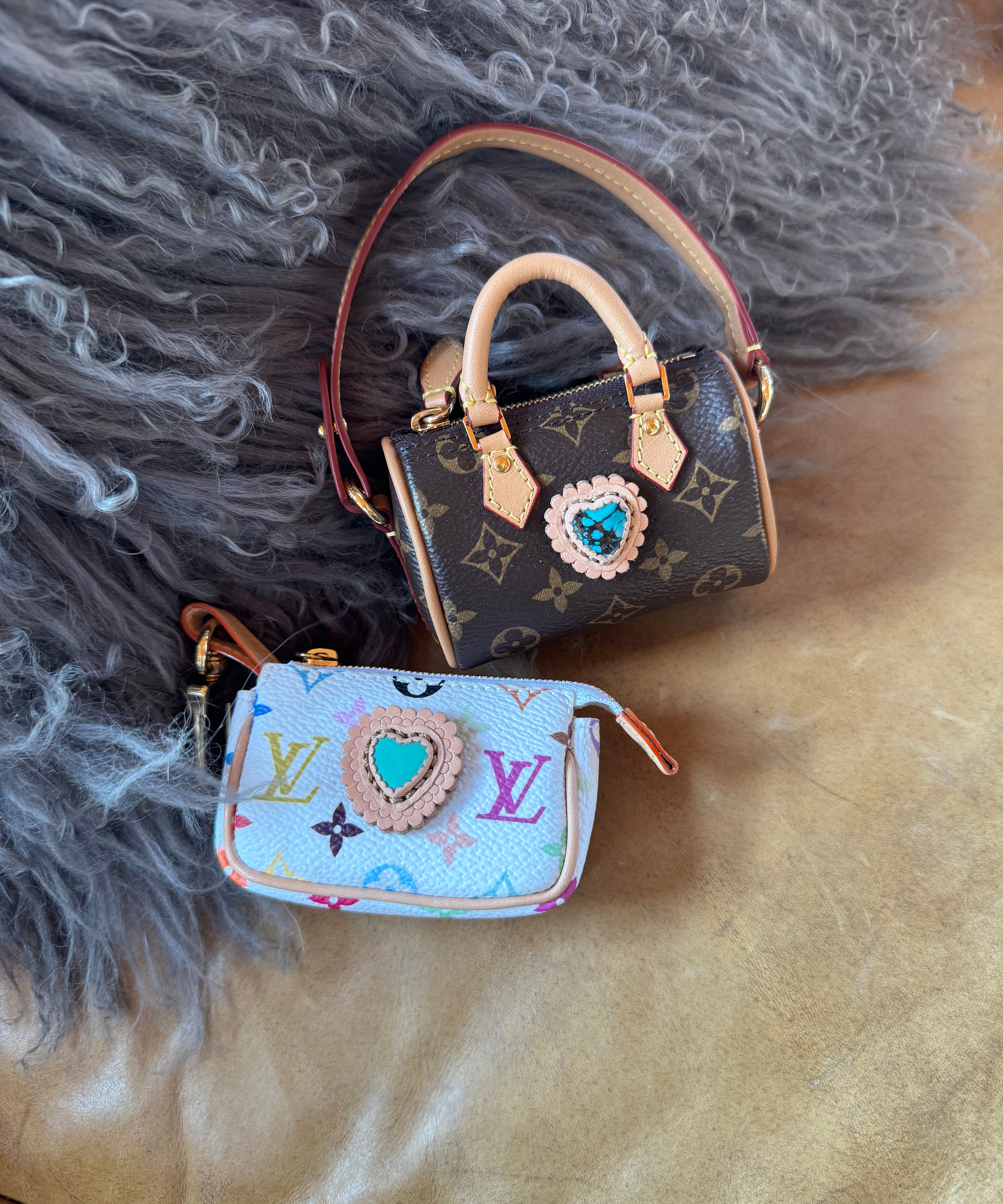 Mini luxury handbag keychain with monogram design adorned with a turquoise gem on textured surface