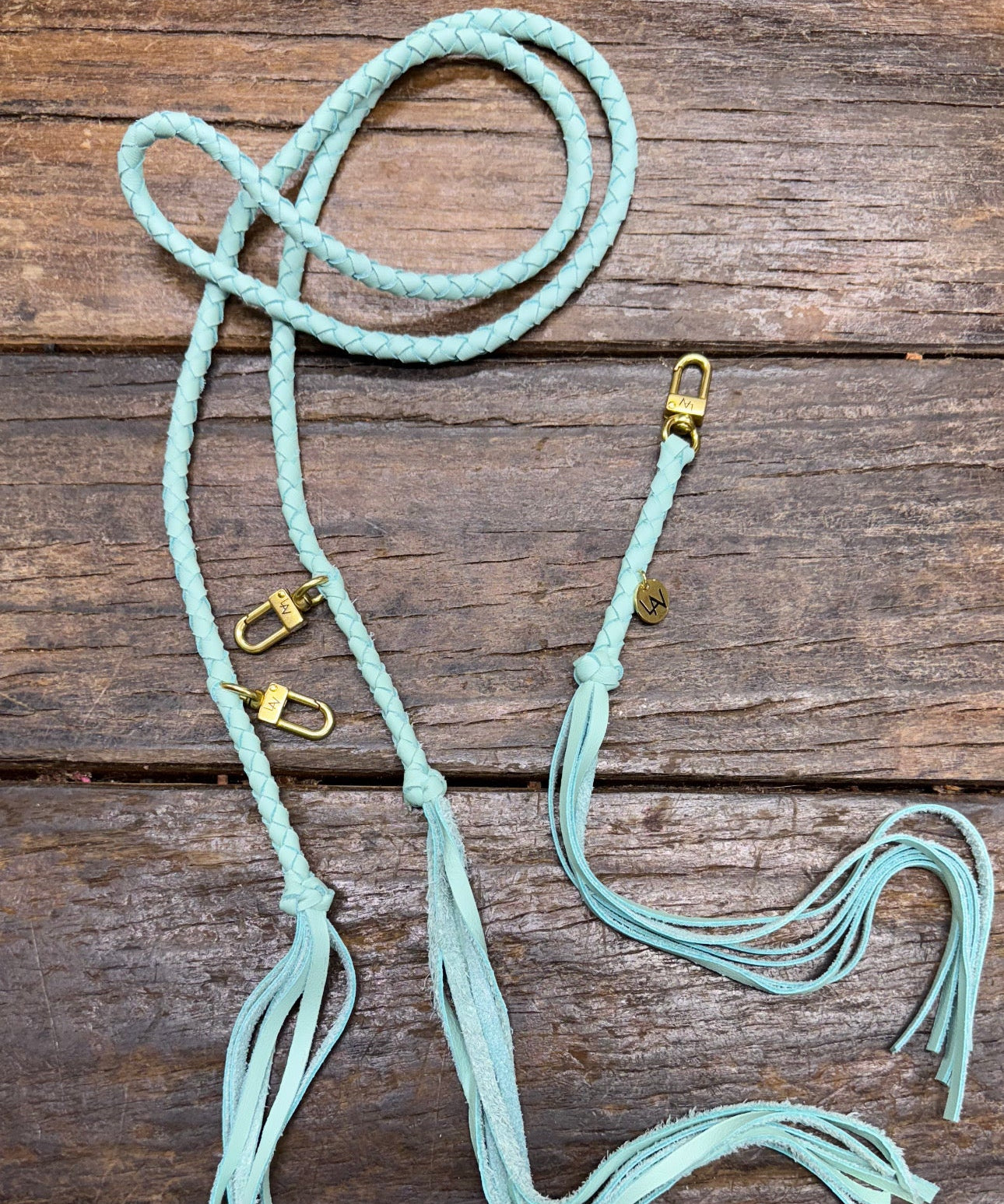 Tiffany blue leather bag strap with gold clasps on a wooden surface