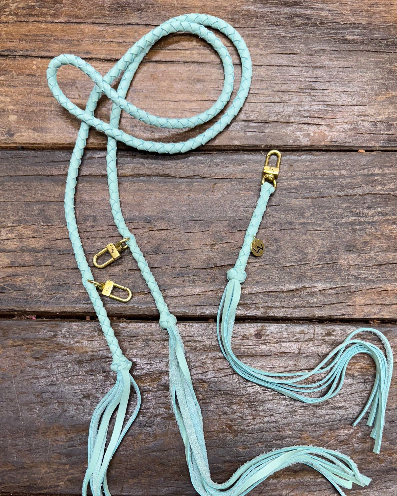 Tiffany blue leather bag strap with gold clasps on a wooden surface