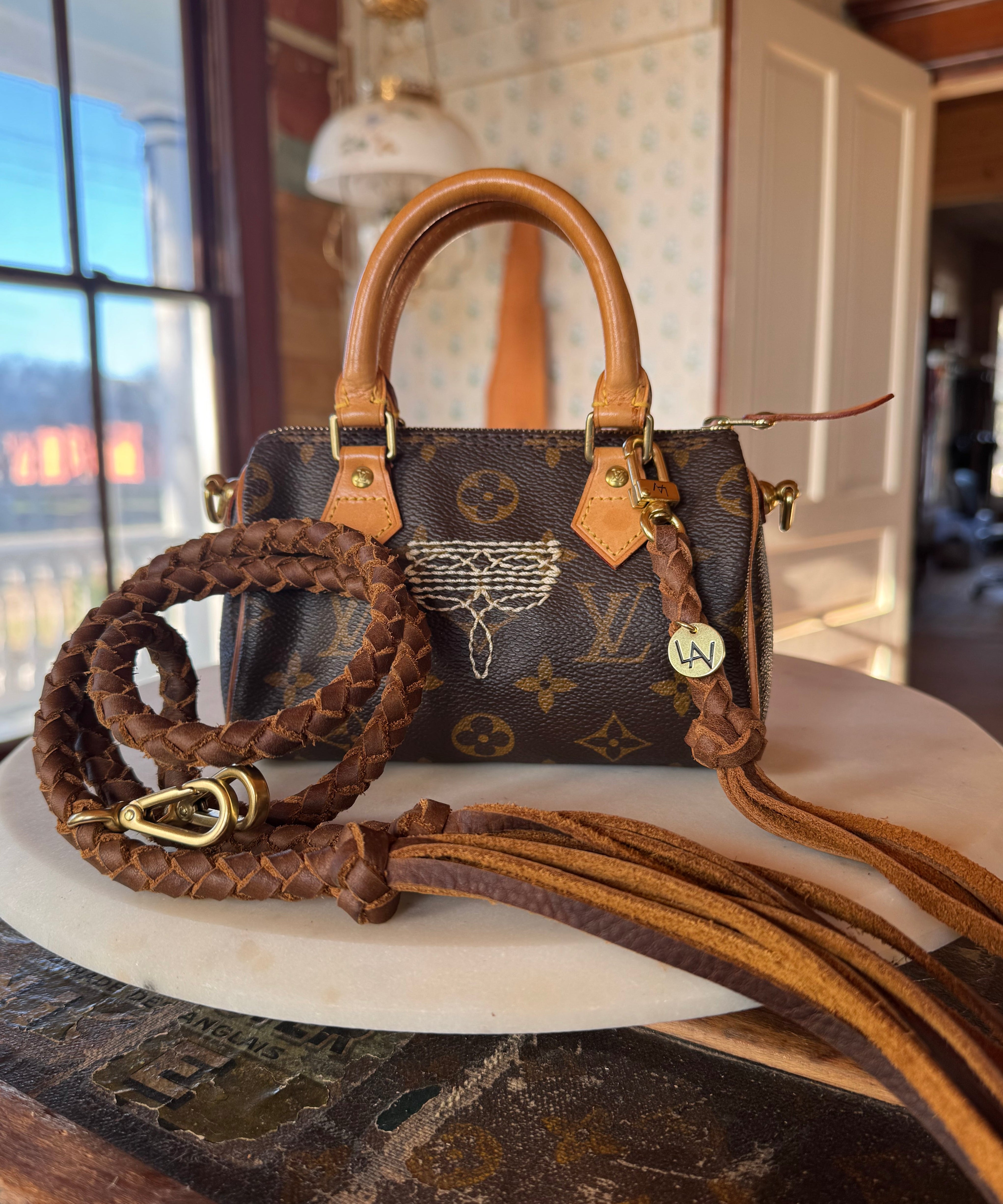 Luxury handbag with monogram pattern, revamped by Leather and Vodka with leather braided straps, sitting on wooden lift