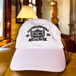 White cap with black logo on a green couch in a room with windows and decor.