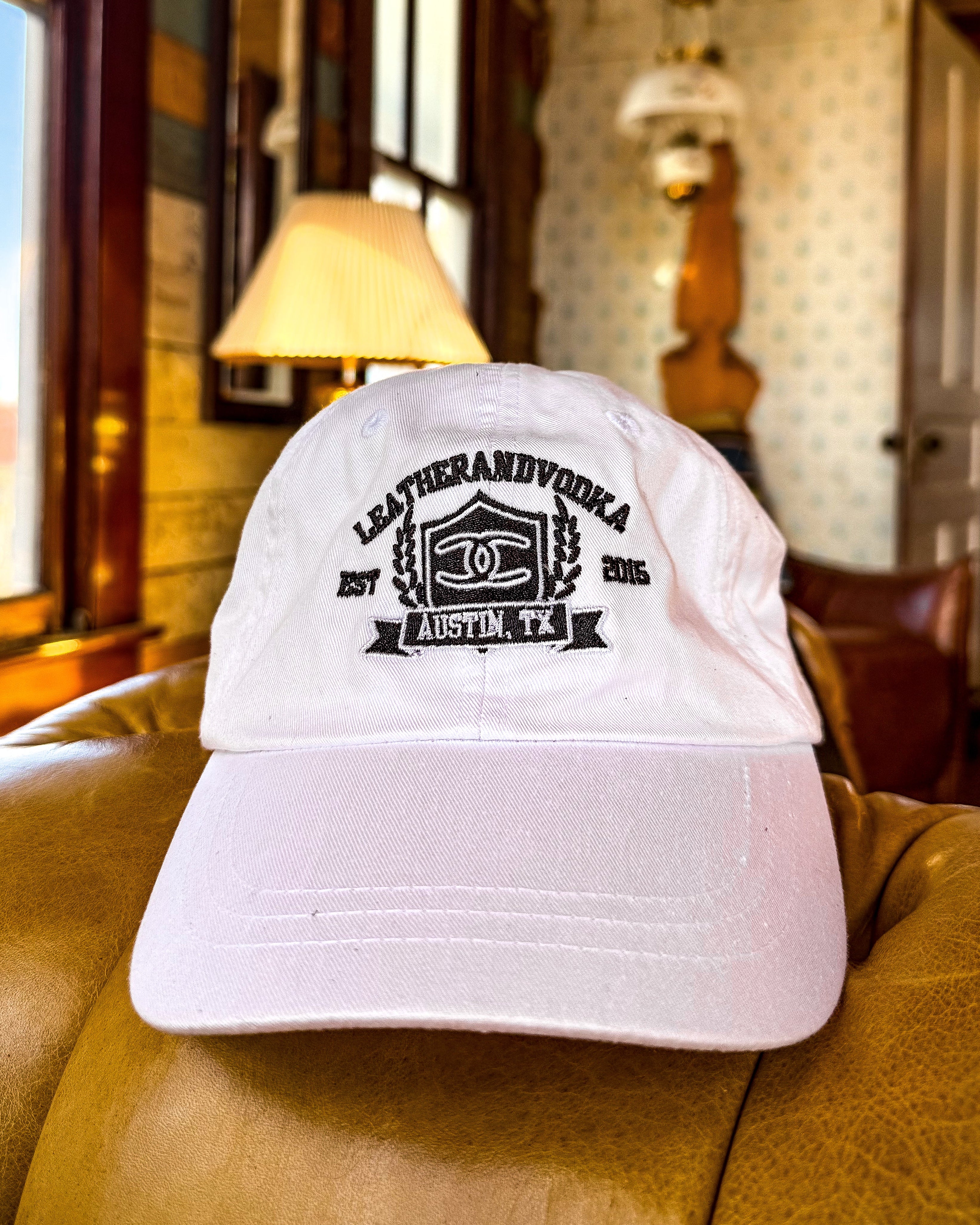 White cap with black logo on a green couch in a room with windows and decor.