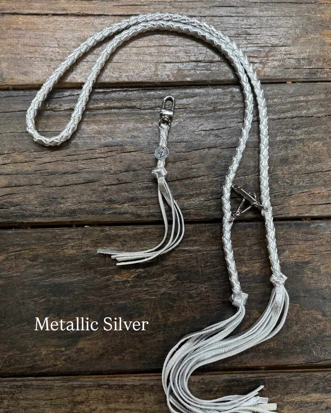 Metallic SIlver Bag Strap, made with braided leather with matching snap on key chain, laying on wooden table. 