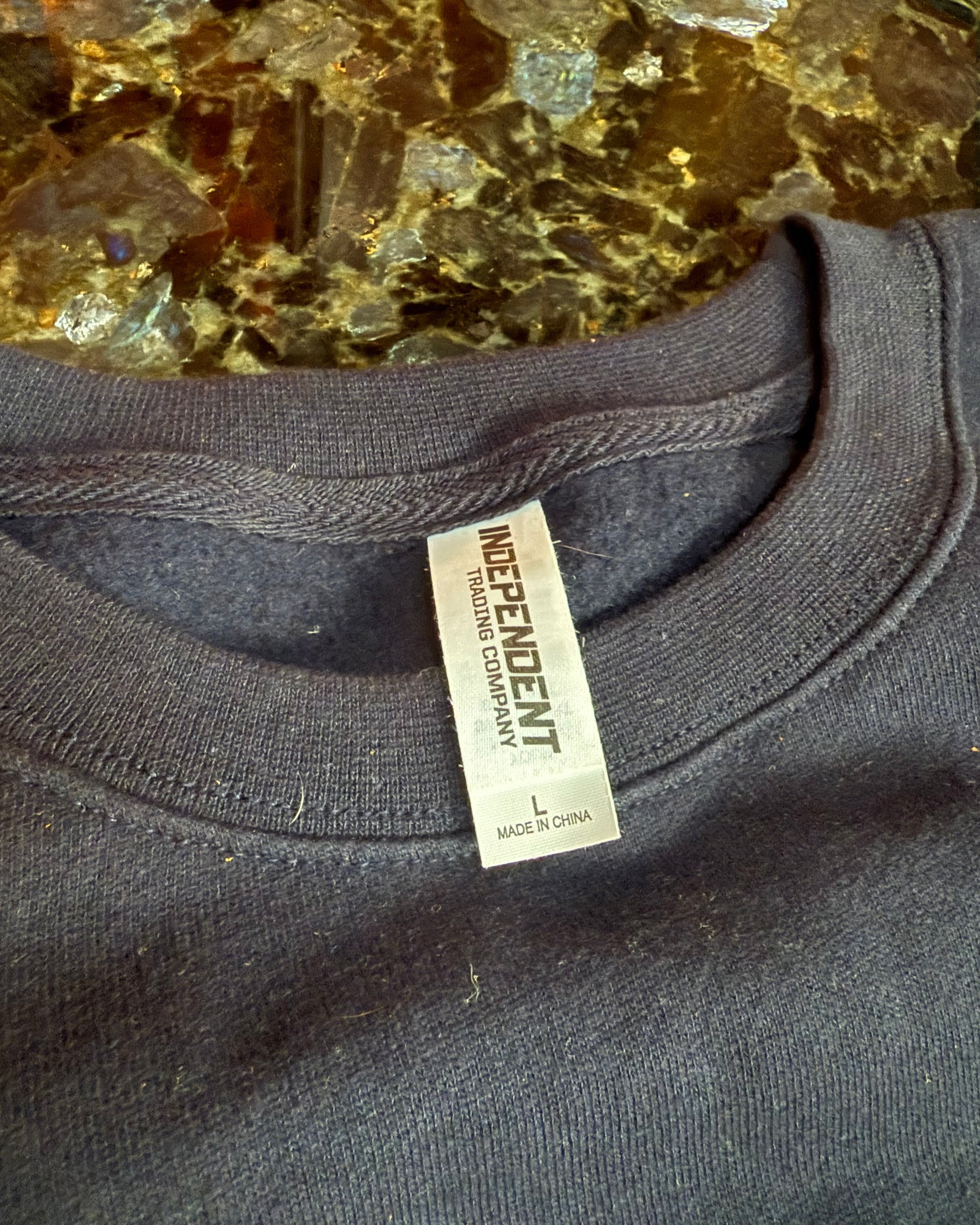 Close-up of a dark gray sweatshirt with an 'Independent Trading Company' label on a textured surface.
