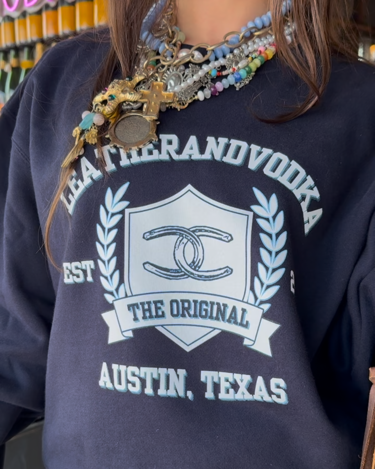 Women wearing blue crewneck with colorful jewelry on at Leatherandvodka in Round Top Texas