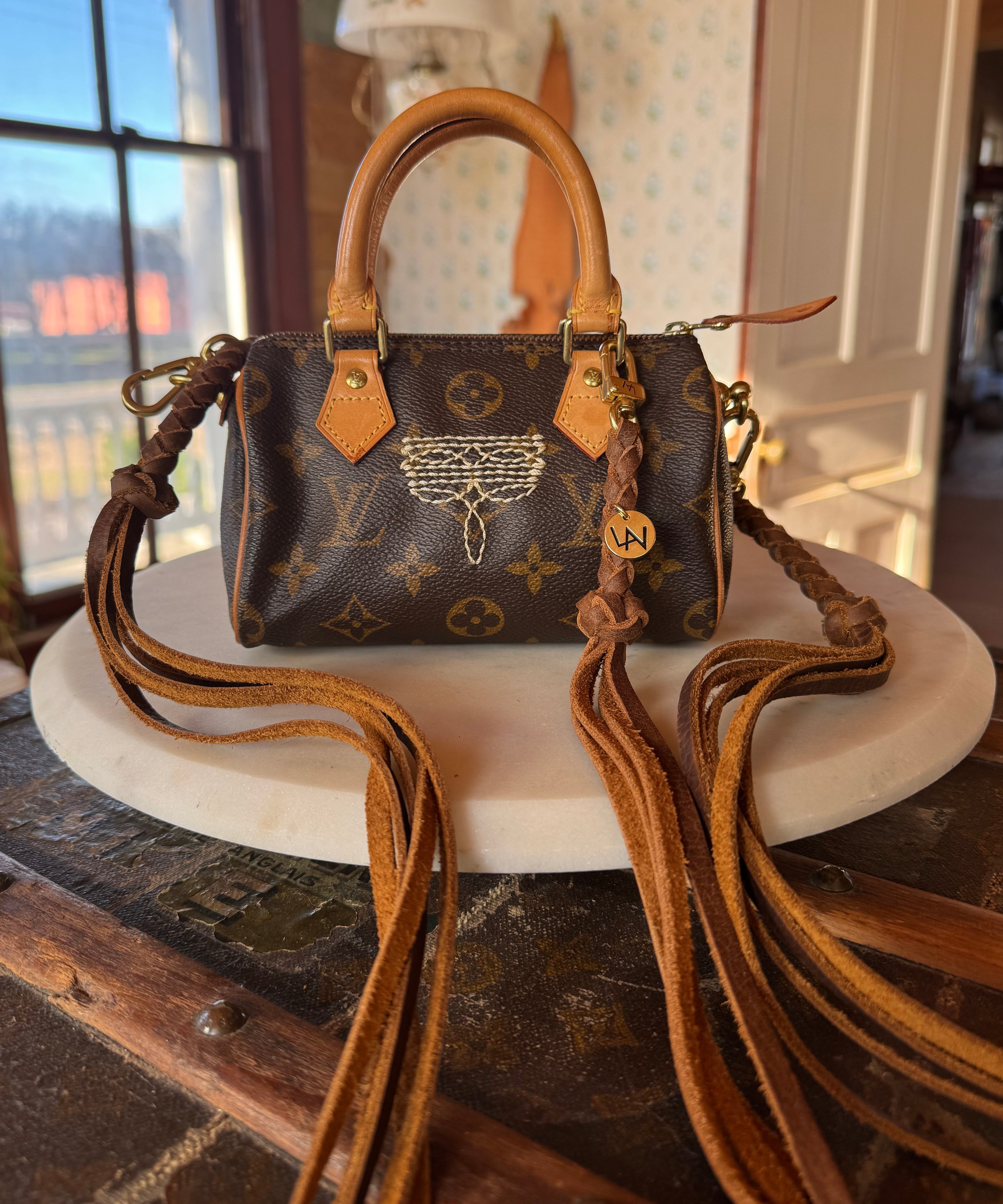 Luxury handbag with monogram pattern, revamped by Leather and Vodka with leather braided straps, sitting on wooden lift