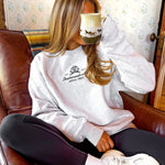 Person wearing a white sweatshirt with text, sitting on a brown leather couch.