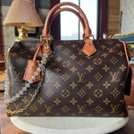 Designer handbag with monogram pattern on a wooden surface. JForks & Leatherandvodka collab, crystal bead and gold chain as a handbag charm.