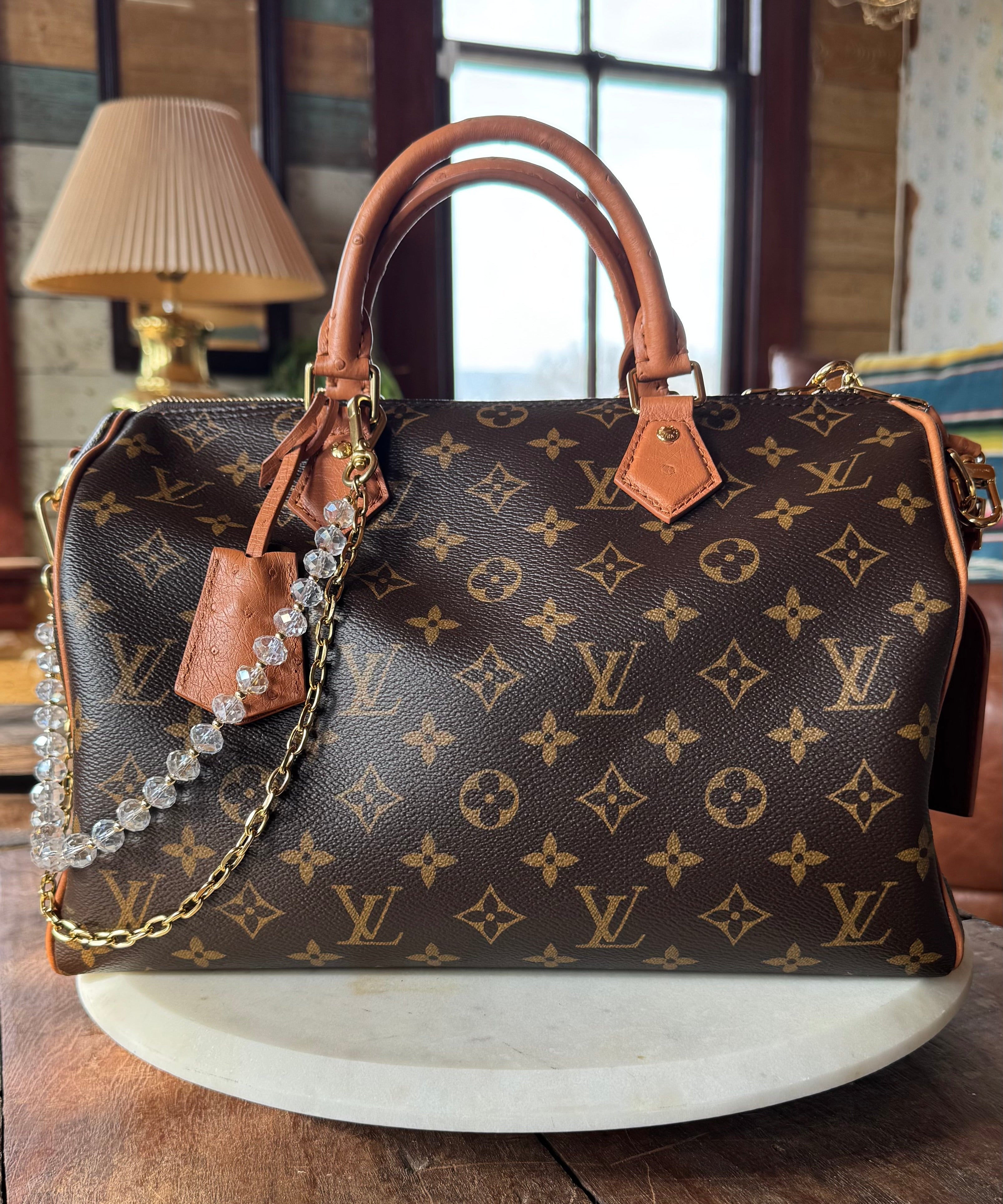 Designer handbag with monogram pattern on a wooden surface. JForks & Leatherandvodka collab, crystal bead and gold chain as a handbag charm.