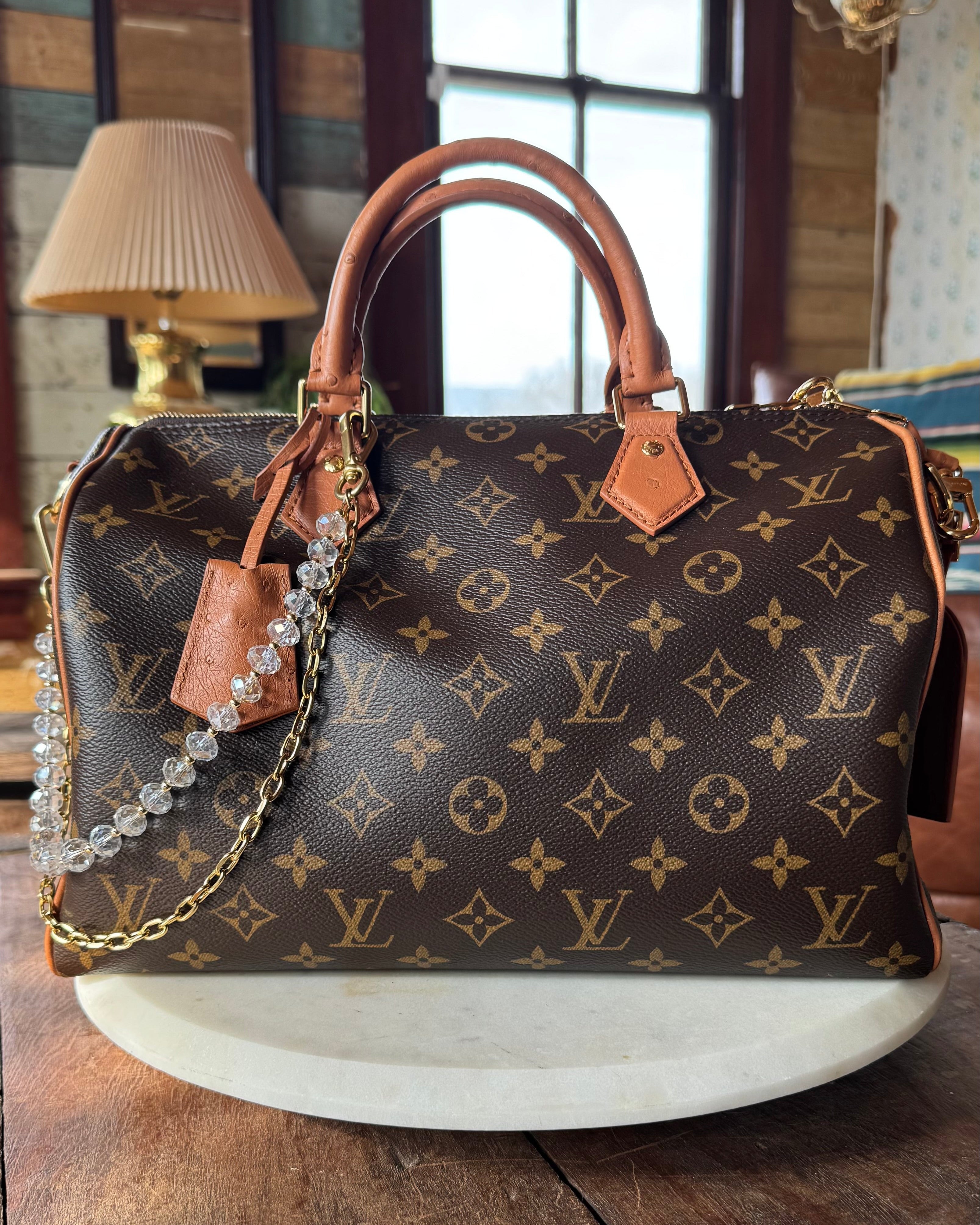 Designer handbag with monogram pattern on a wooden surface. JForks & Leatherandvodka collab, crystal bead and gold chain as a handbag charm.