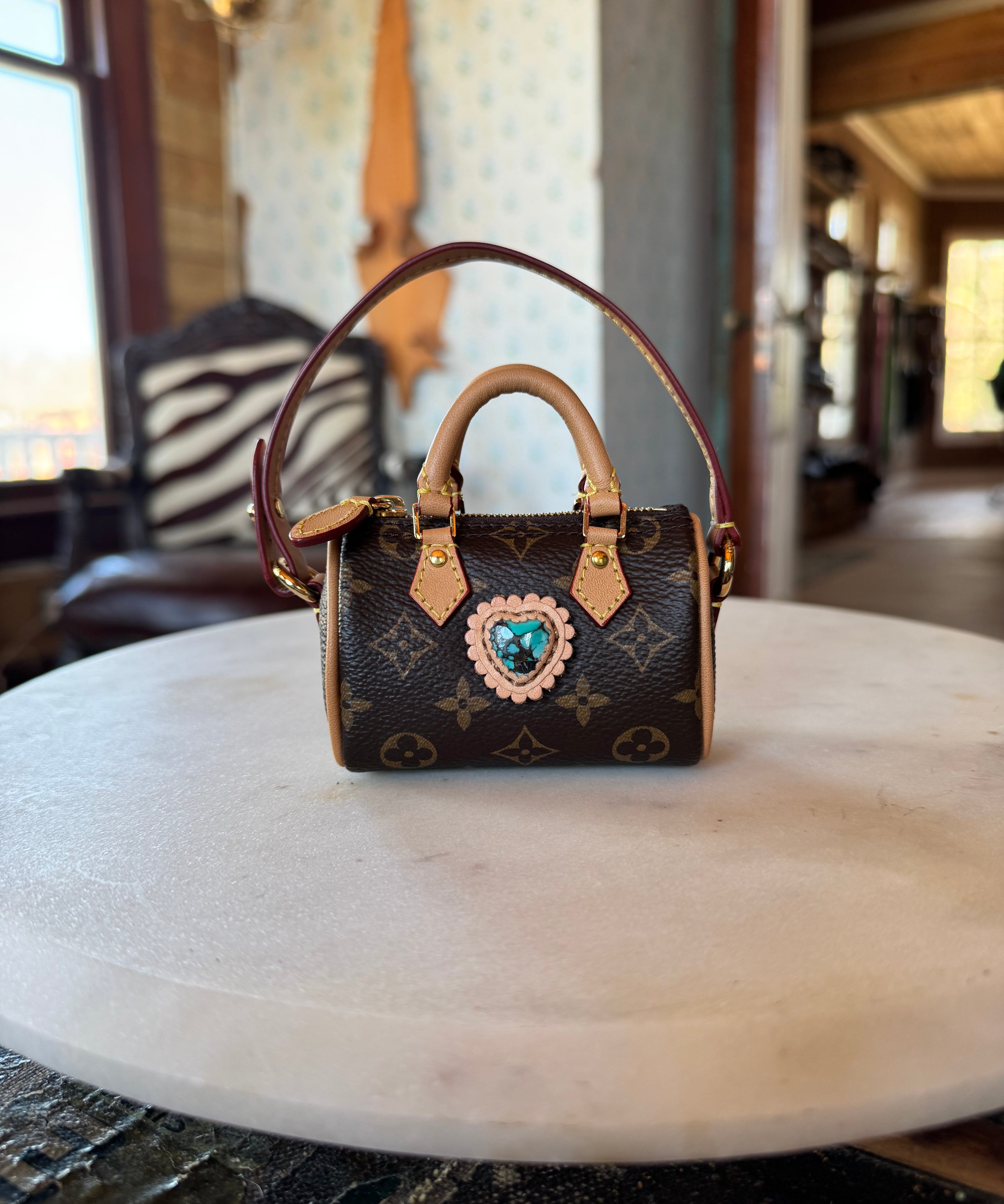 Mini luxury handbag keychain with monogram design with turquoise gem on a marble surface