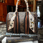 Designer handbag with a pink, white, black and yellow patterned twilly on a marble surface.