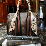 Designer handbag with a pink, white, black and yellow patterned twilly on a marble surface.