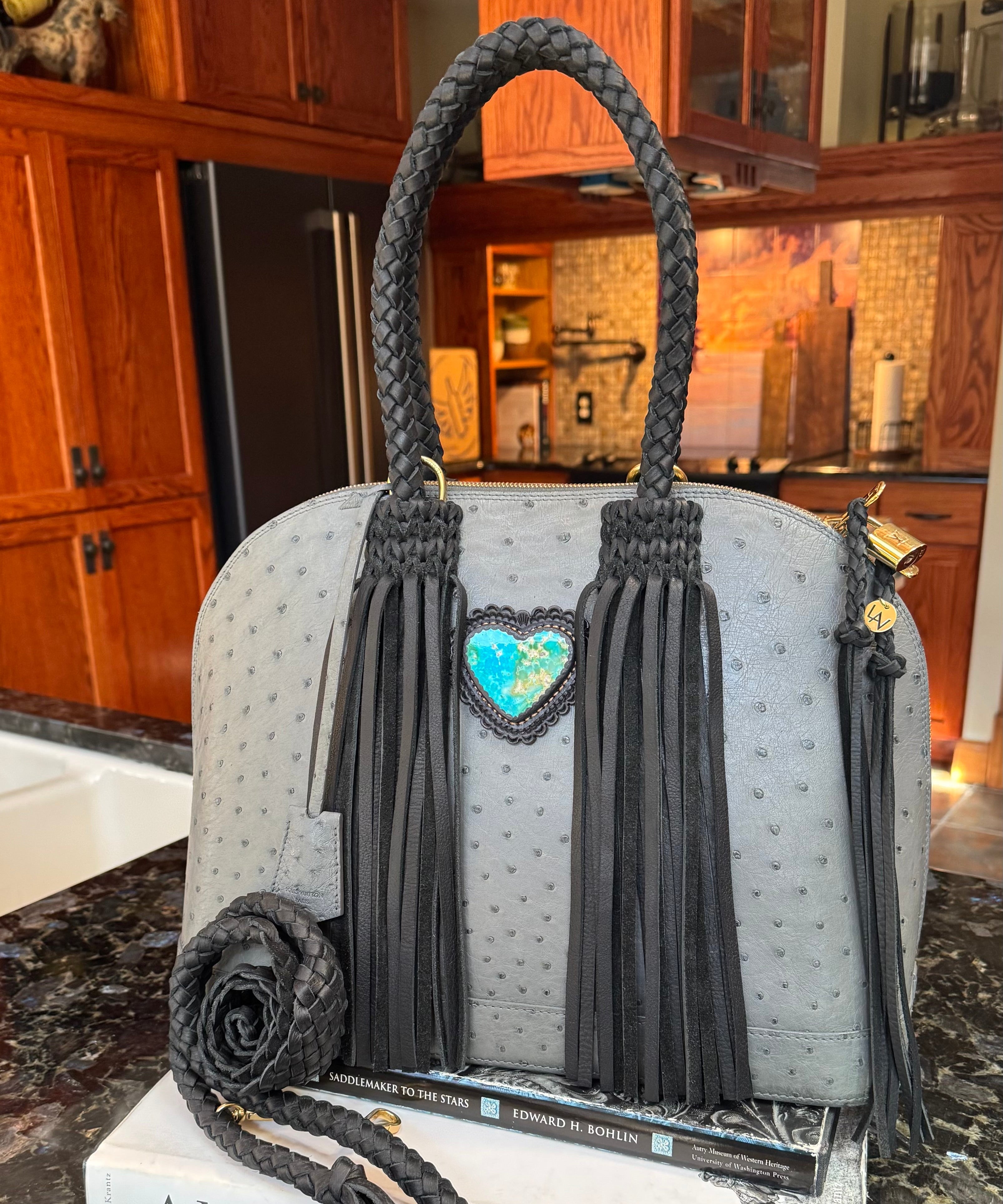 Gray handbag with black tassels and a heart-shaped charm on a kitchen counter.