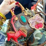 Luxury handbag with decorative charms held by a hand, with camouflage fabric in the background.