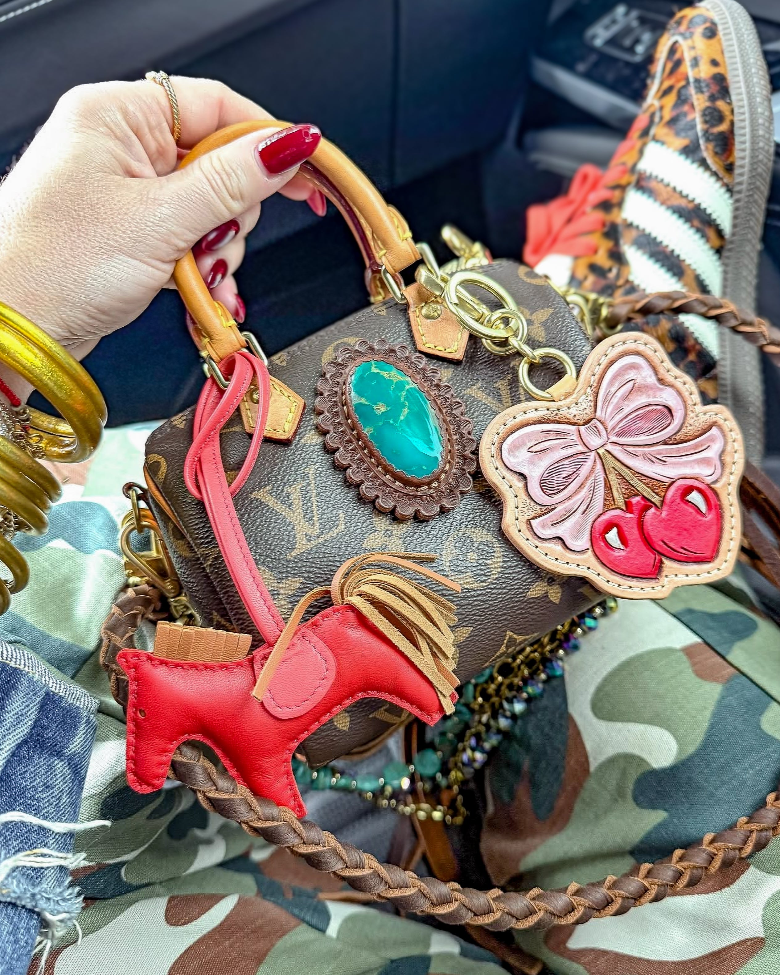 Luxury handbag with decorative charms held by a hand, with camouflage fabric in the background.